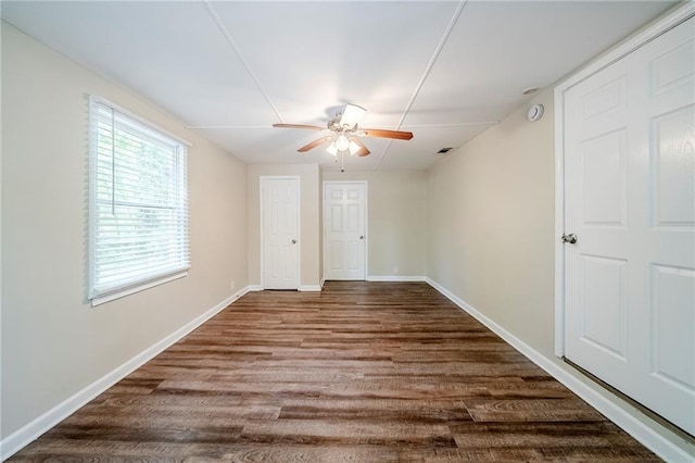 empty room with a ceiling fan, visible vents, baseboards, and dark wood finished floors