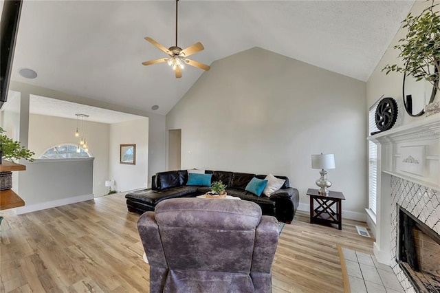 living room with ceiling fan, light wood-type flooring, a fireplace, and high vaulted ceiling