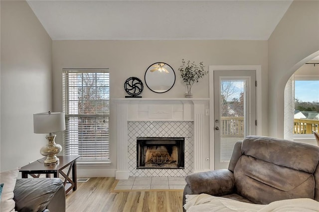 living area with a tile fireplace, lofted ceiling, and light wood-type flooring