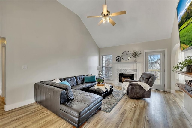 living room featuring high vaulted ceiling, ceiling fan, light wood-type flooring, and a tile fireplace