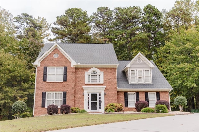 view of front facade with roof with shingles, brick siding, and a front lawn