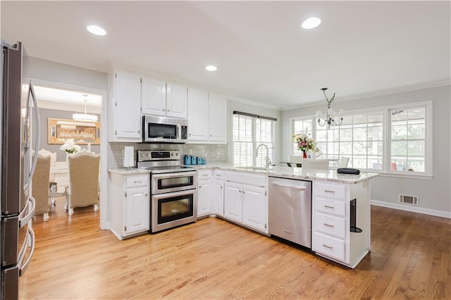 kitchen with visible vents, a peninsula, an inviting chandelier, stainless steel appliances, and crown molding