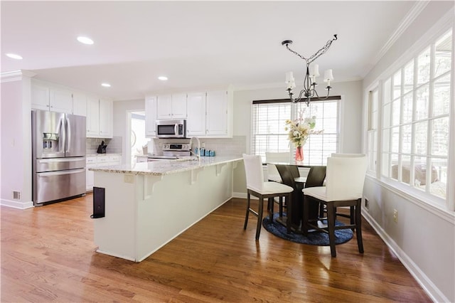 kitchen featuring stainless steel appliances, light wood-style flooring, ornamental molding, white cabinetry, and a peninsula