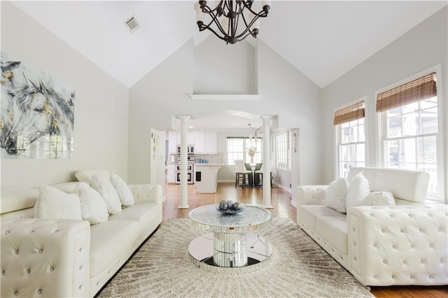 living room featuring decorative columns, high vaulted ceiling, visible vents, a chandelier, and light wood-type flooring