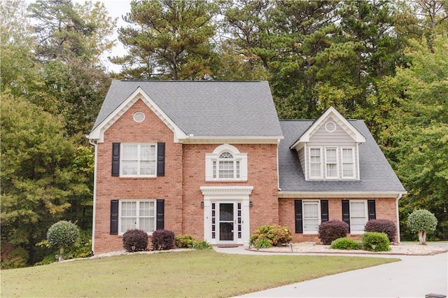 view of front of property with a front lawn, a shingled roof, and brick siding