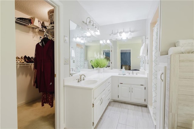 full bathroom with double vanity, a spacious closet, and a sink