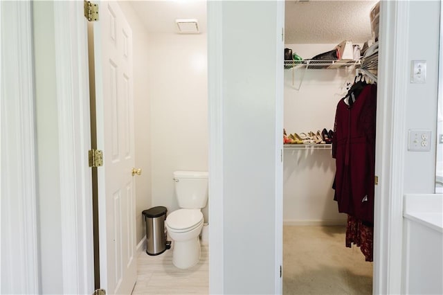 bathroom featuring a textured ceiling, a spacious closet, toilet, and baseboards