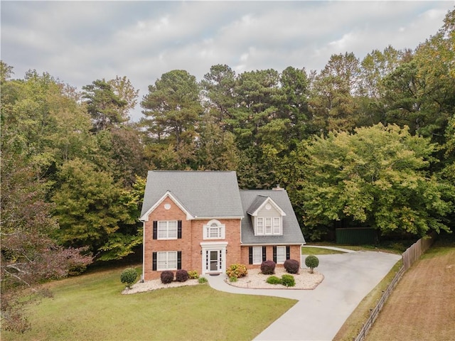 colonial house with a front yard, brick siding, fence, and driveway