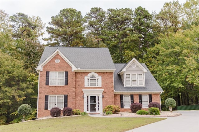 colonial-style house featuring brick siding, a front lawn, and a shingled roof