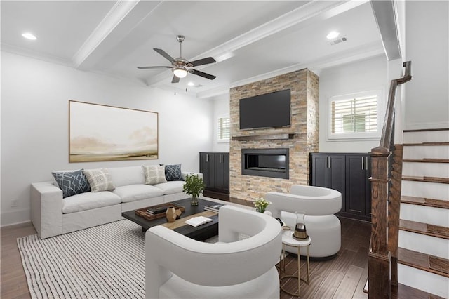 living room with ceiling fan, dark hardwood / wood-style flooring, beamed ceiling, and a stone fireplace