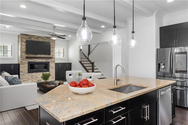 kitchen featuring beam ceiling, a wealth of natural light, an island with sink, and a stone fireplace