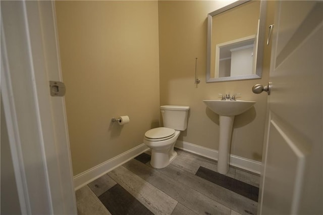 half bath featuring toilet, a sink, baseboards, and wood finished floors