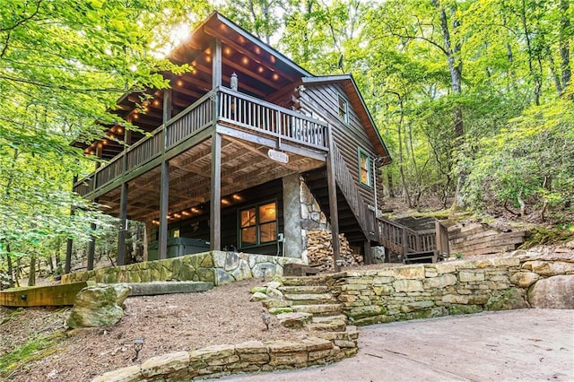 rear view of house featuring stone siding, stairs, and a deck