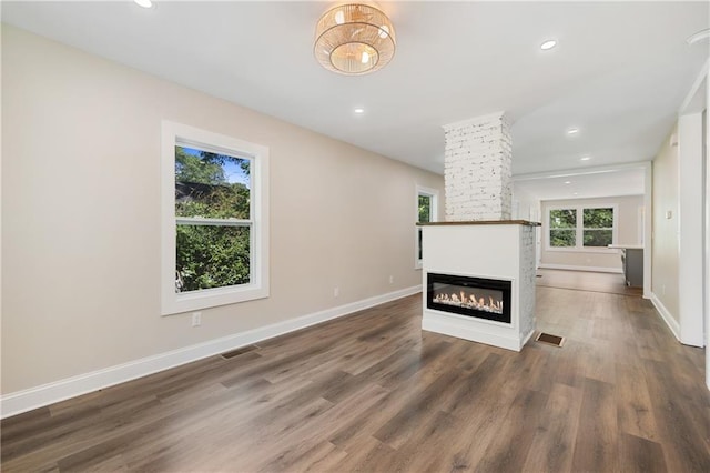 unfurnished living room with a fireplace, decorative columns, and dark wood-type flooring