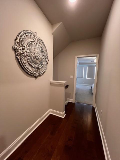 hallway with lofted ceiling, baseboards, dark wood finished floors, and an upstairs landing