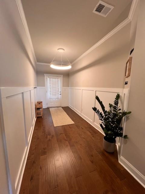 interior space with visible vents, wainscoting, dark wood-style flooring, crown molding, and a decorative wall