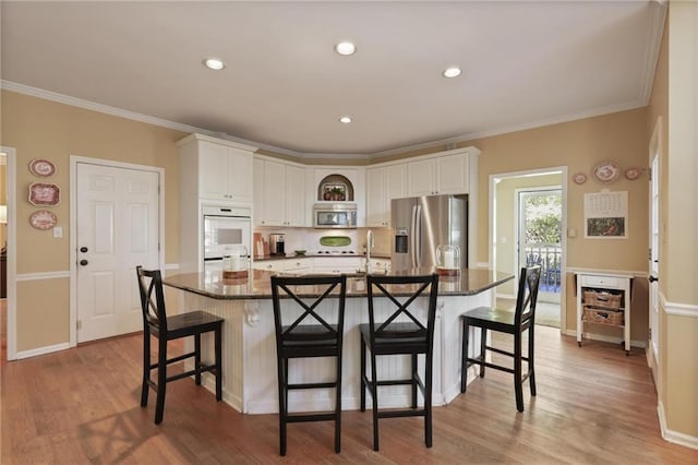 kitchen with appliances with stainless steel finishes, dark stone countertops, a breakfast bar area, white cabinetry, and a large island