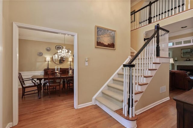 stairway with hardwood / wood-style flooring, a brick fireplace, crown molding, and a notable chandelier