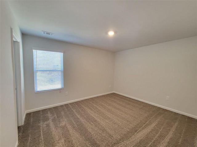 empty room featuring dark carpet, visible vents, and baseboards