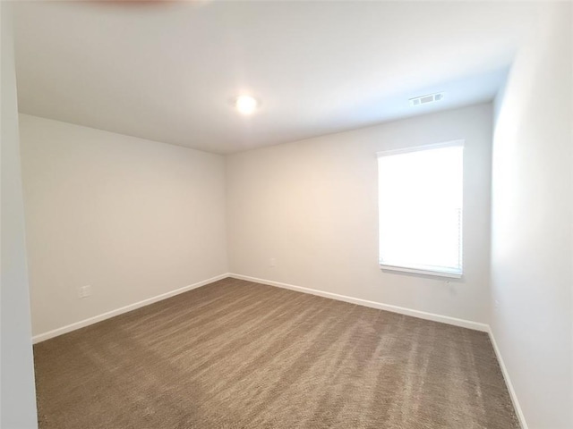 unfurnished room featuring dark colored carpet, visible vents, and baseboards