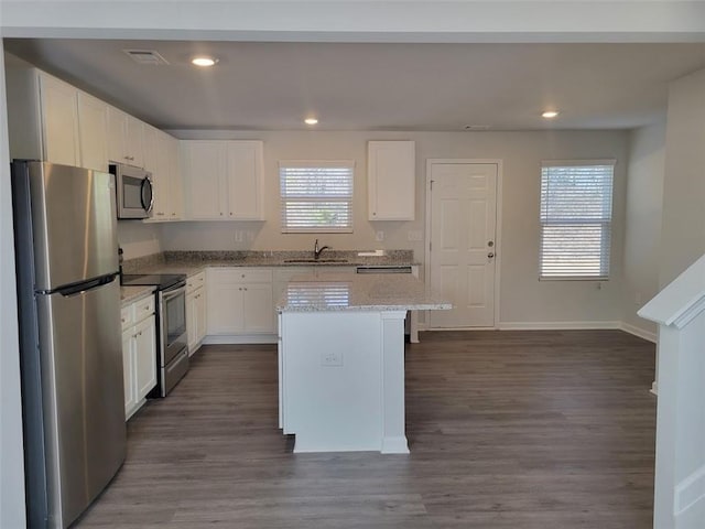 kitchen featuring light stone counters, appliances with stainless steel finishes, white cabinetry, and a center island