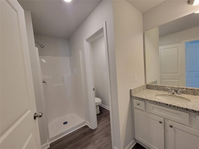 bathroom with a stall shower, wood finished floors, toilet, and baseboards