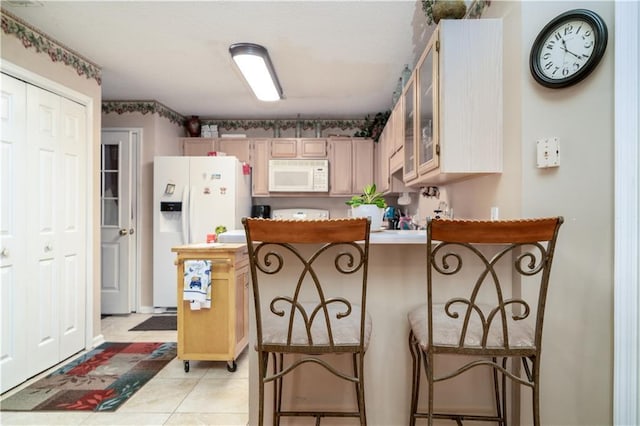 kitchen featuring white appliances, a kitchen breakfast bar, light brown cabinetry, and light tile patterned floors