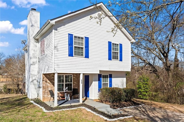 view of front of property with a front yard, a patio area, a chimney, and brick siding