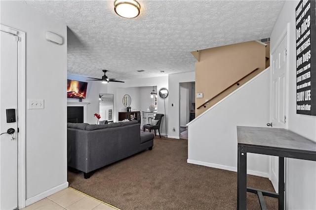 carpeted living area with ceiling fan, a textured ceiling, a fireplace, baseboards, and stairs