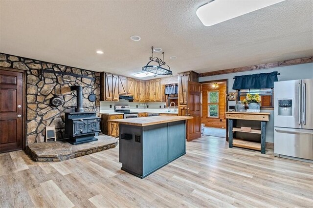 kitchen with a wood stove, stainless steel appliances, under cabinet range hood, wooden counters, and a sink