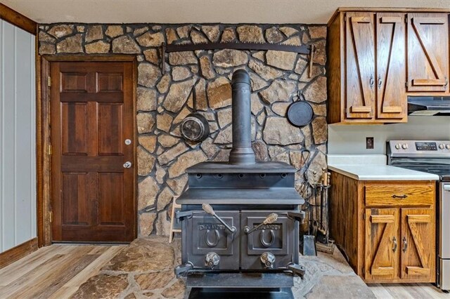 interior details featuring wood finished floors, a wood stove, stainless steel electric range, and exhaust hood