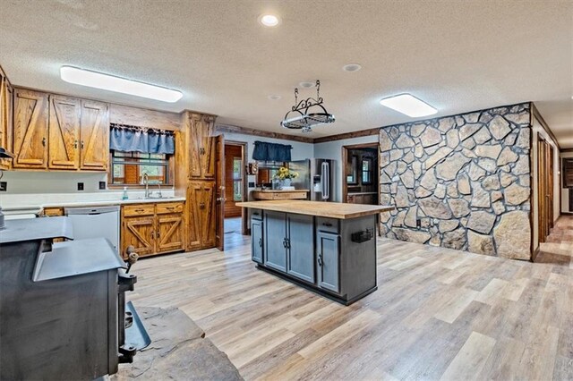 kitchen featuring a textured ceiling, a sink, a kitchen island, light wood-type flooring, and dishwasher