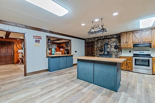 kitchen featuring a wood stove, electric range, light wood-style flooring, and exhaust hood