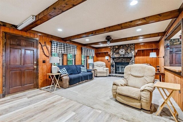 living area with a fireplace, a textured ceiling, wooden walls, wood finished floors, and beamed ceiling