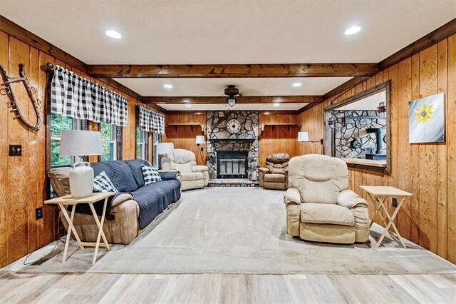 living room featuring beam ceiling, a fireplace, wooden walls, a textured ceiling, and wood finished floors