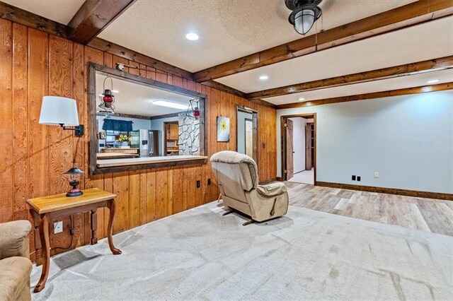 sitting room featuring baseboards, wood finished floors, a textured ceiling, wood walls, and beam ceiling