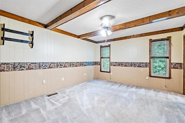 spare room with visible vents, ceiling fan, a textured ceiling, carpet flooring, and beam ceiling