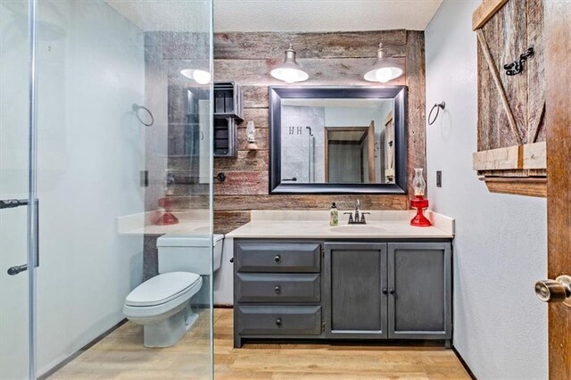 full bathroom featuring toilet, a shower with door, wood finished floors, and vanity