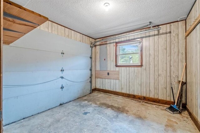 garage featuring wood walls, electric panel, and baseboards