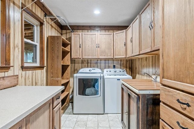 clothes washing area with washing machine and dryer, cabinet space, and wooden walls