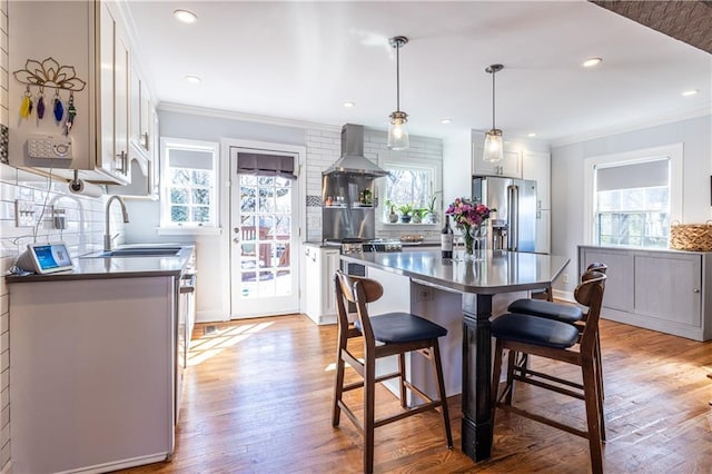 kitchen featuring a sink, high end appliances, wall chimney exhaust hood, and light wood finished floors