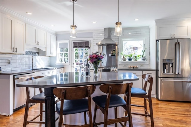 kitchen featuring dark countertops, light wood finished floors, wall chimney range hood, appliances with stainless steel finishes, and a sink