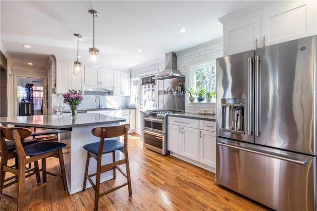 kitchen featuring light wood finished floors, tasteful backsplash, crown molding, appliances with stainless steel finishes, and wall chimney exhaust hood