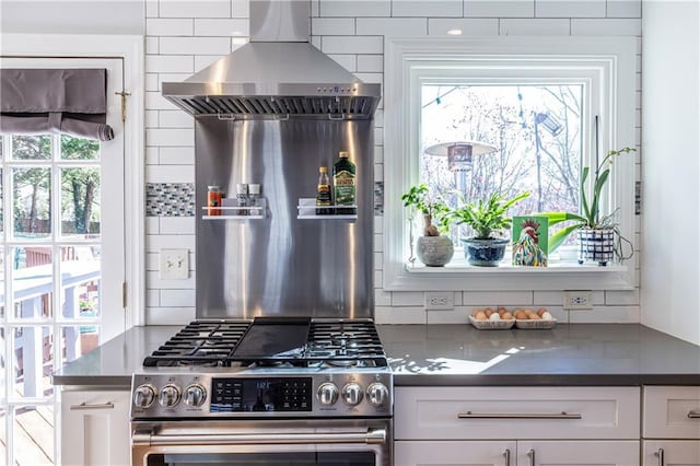 kitchen with dark countertops, backsplash, extractor fan, stainless steel gas range, and white cabinetry