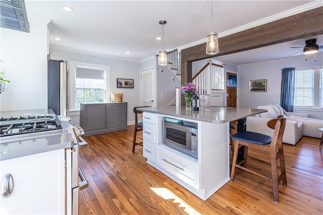 kitchen with ornamental molding, stainless steel appliances, light wood-style floors, a kitchen bar, and open floor plan