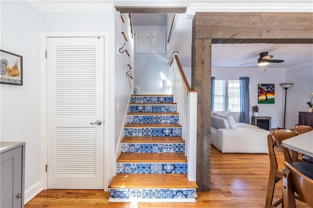 stairs with crown molding, ceiling fan, and wood finished floors