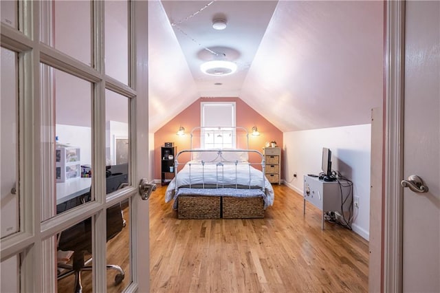 bedroom with lofted ceiling, baseboards, and light wood finished floors