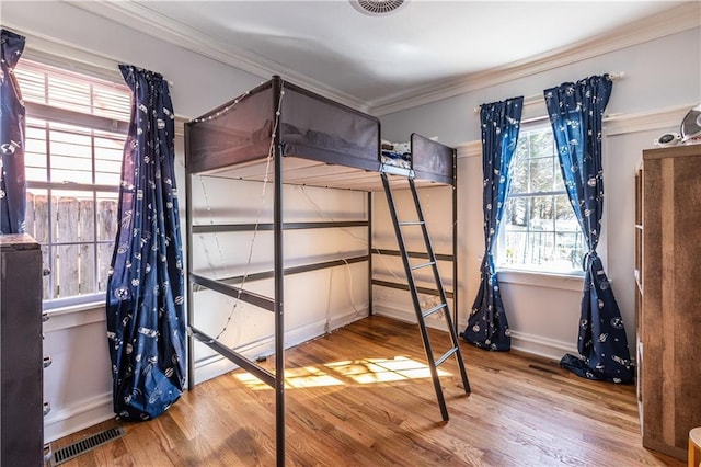 bedroom featuring wood finished floors, visible vents, and ornamental molding