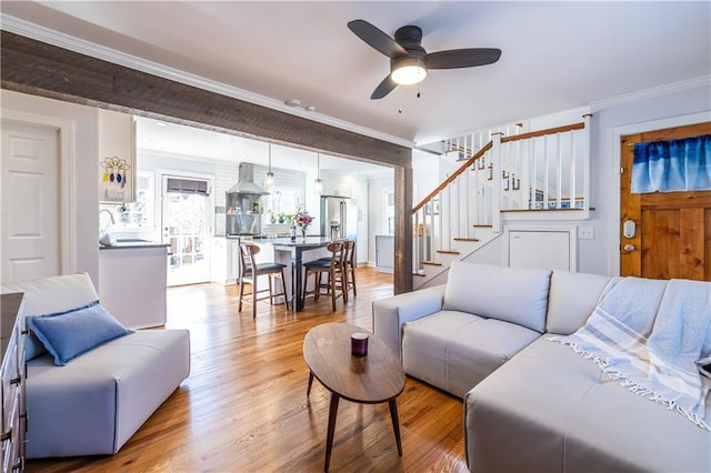 living room with crown molding, stairway, a ceiling fan, and light wood finished floors