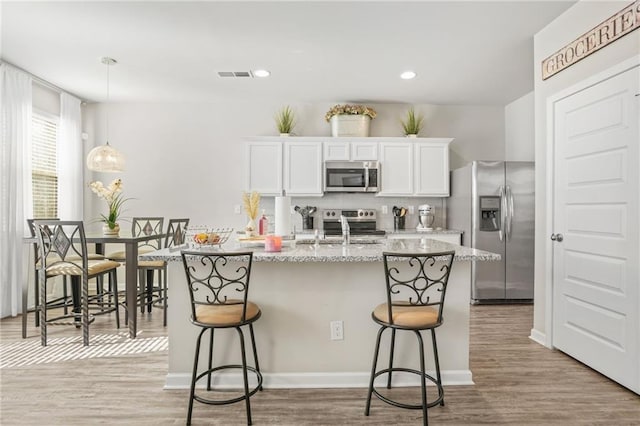 kitchen featuring sink, a breakfast bar area, appliances with stainless steel finishes, light stone countertops, and white cabinets